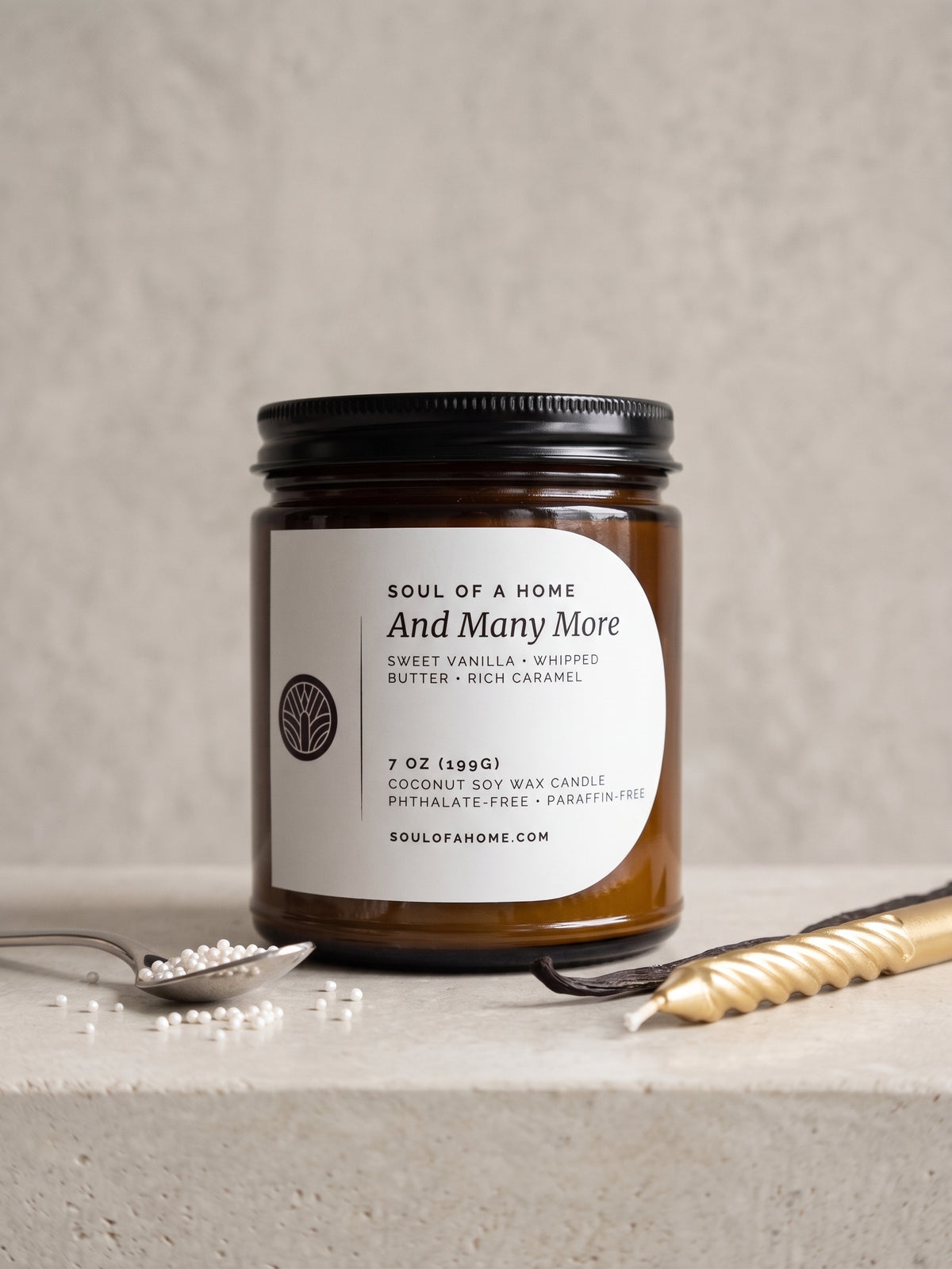 A 7 oz soy wax candle in an amber glass jar with a black lid and a white label reading 'Soul of a Home And Many More', styled on a light stone surface with a spoon with cake sprinkles, a vanilla bean, and a gold birthday candle.