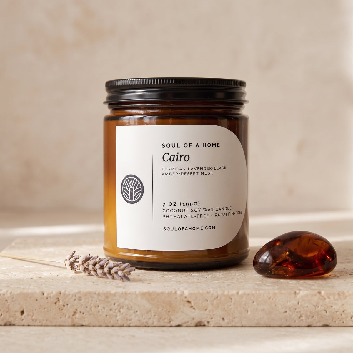 A 7 oz soy wax candle in an amber glass jar with a black lid and a white label reading 'Soul of a Home Cairo'. The jar sits on a light stone surface with a lavender sprig and a polished amber stone nearby, against a warm beige background.