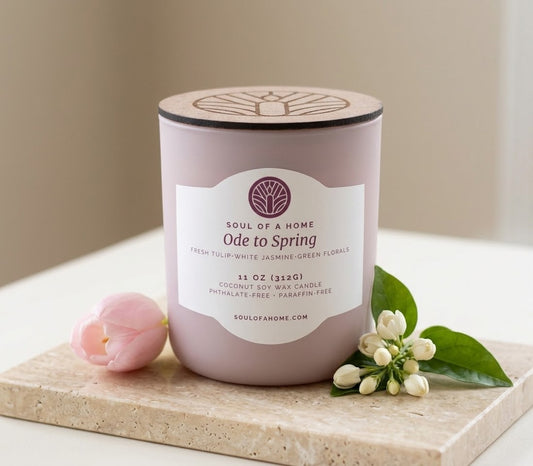 A floral coconut soy wax candle in a glass blush colored jar with a matching lid, labeled 'Soul of a Home Ode to Spring', styled on a stone tray with a pink tulip and white jasmine flowers.